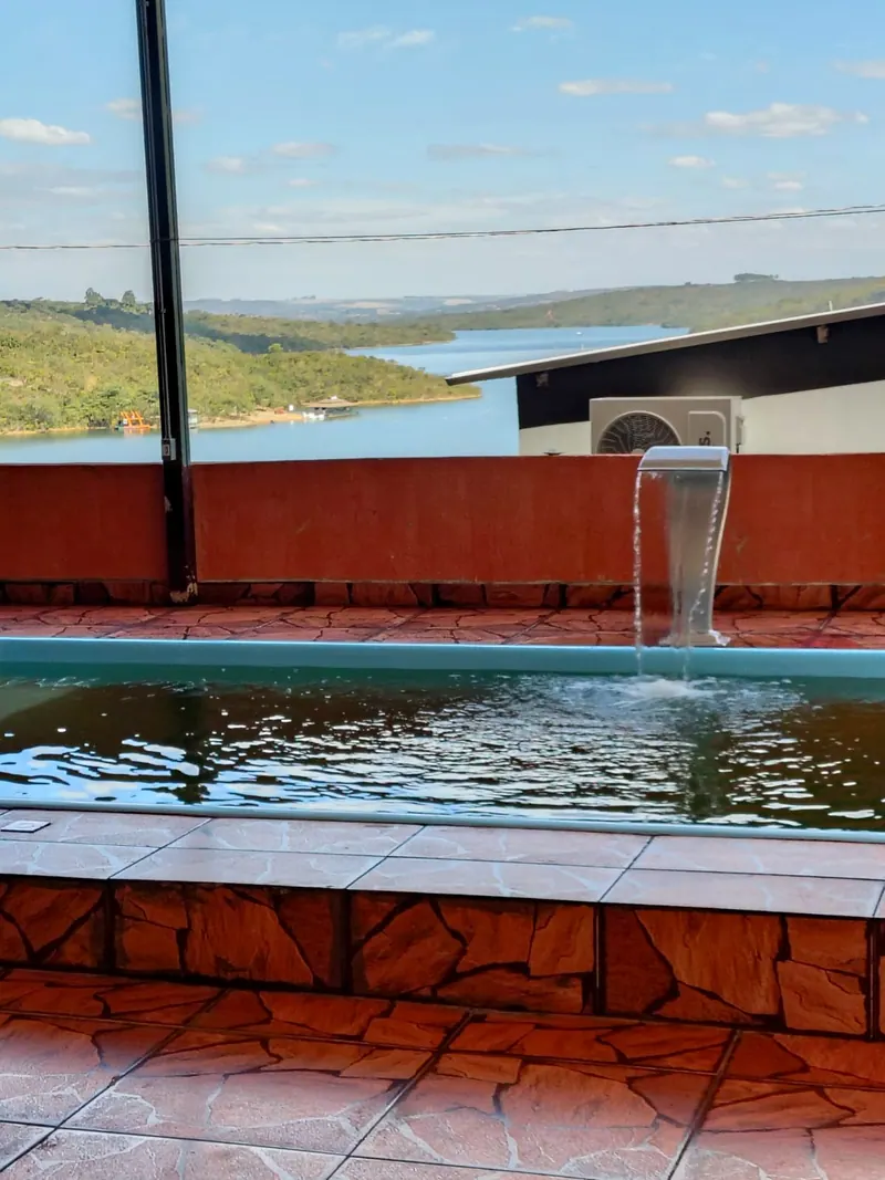 Piscina com queda d'água e, ao fundo, a vista do lago Corumbá IV entre os morros