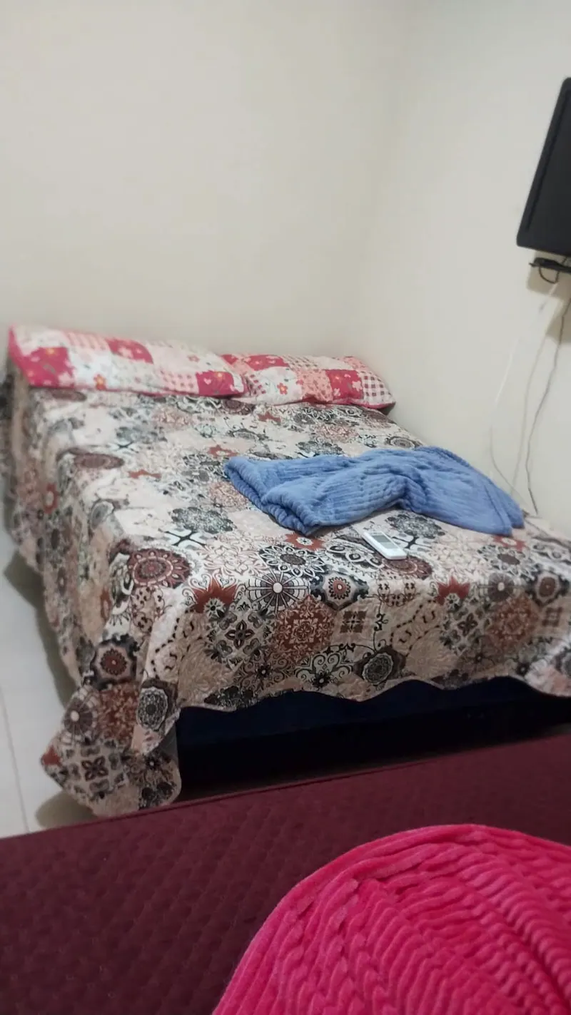 Suíte com cama de casal de colcha florida e uma toalha azul dobrada em laço